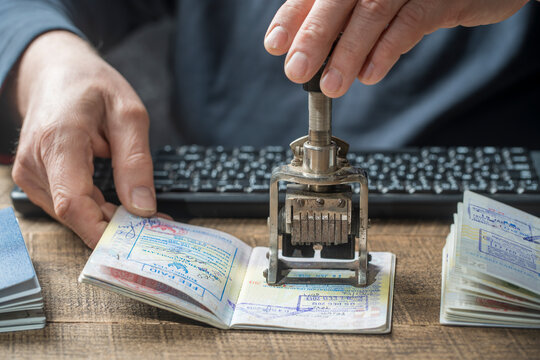 Immigration and passport control at the airport. Man border control officer puts a stamp in the international passport, closeup. Vacation and travel concept