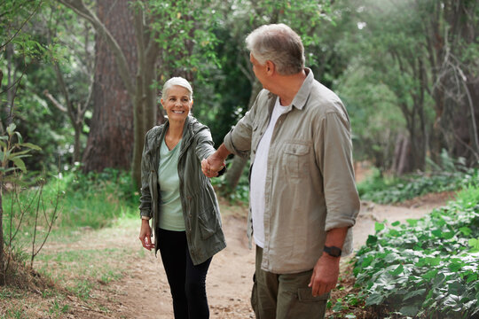 Elderly couple, holding hands and hiking in a forest, happy and relax while walking in nature. Senior, backpacker and woman with man outdoors for travel, freedom and healthy lifestyle in retirement