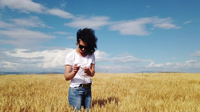 Slow motion of a happy young woman holding ear of wheat in golden wheat field in summer