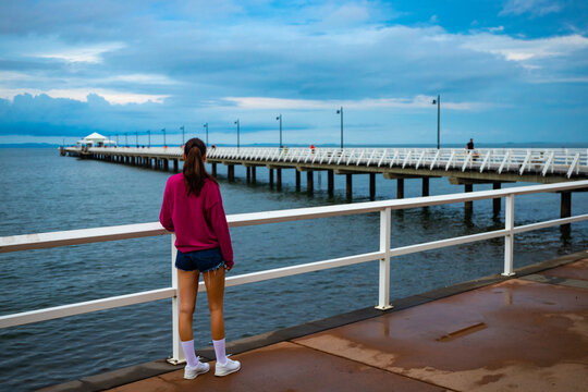 A beautiful girl in a pink blouse looks out over the famous stunning long white Shorncliffe pier in Brisbane, Queensland, Australia