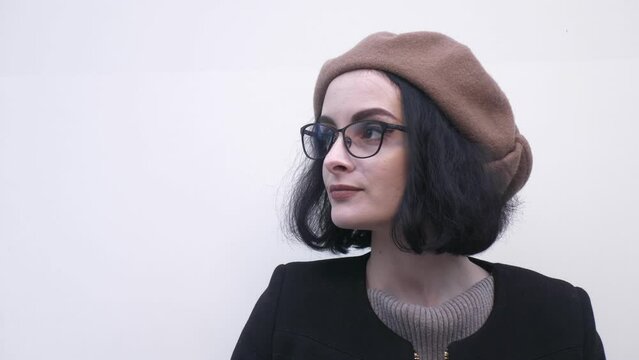 Video portrait. A young woman in a beret and glasses against a white wall. Stylish young lady. Creative person.