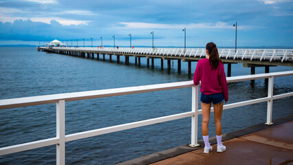 A beautiful girl in a pink blouse looks out over the famous stunning long white Shorncliffe pier in...