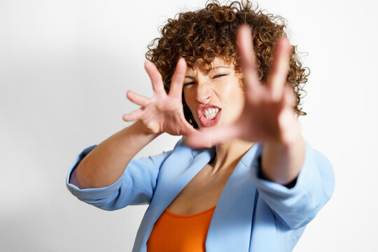 Woman with curly hair making face and gesturing against white background