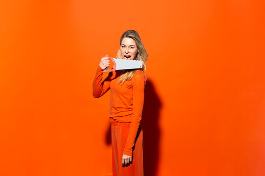 Woman with mouth open holding hand saw against orange background