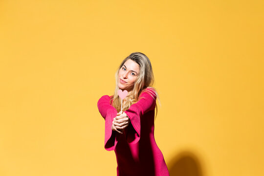 Smiling woman giving heart paper sign against yellow background