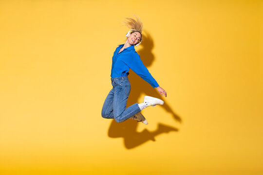 Carefree woman jumping in joy against yellow background