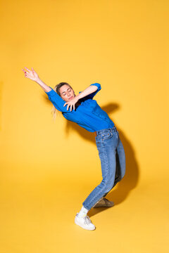 Carefree woman dancing with hand raised against yellow background