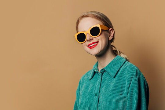 Happy woman wearing sunglasses standing against brown background