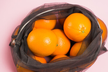 Oranges in a reusable grid on a pink background. Concept of earth day, zero waste and recycling