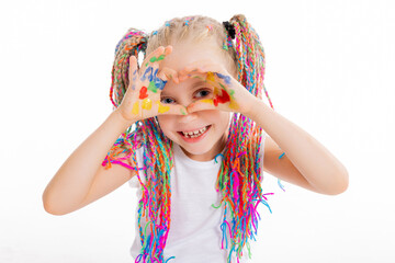 Adorable school kid girl with colorful pgtails sitting on white floor in studio isolated posing for back to school concept holds colorful painted hands in heart shape showing at camera in good mood.