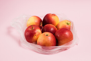 Red apples in a transparent plastic bag on a pink paper background. Concept of earth day, zero waste and recycling