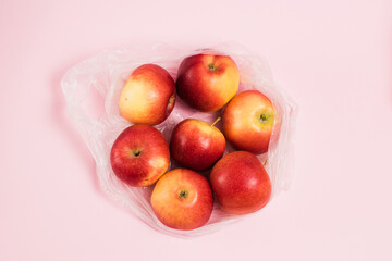Red apples in a transparent plastic bag on a pink paper background. Concept of earth day, zero...