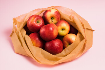 Red apples in a reusable fruit and vegetable bag on a pink paper background. Concept of earth day, zero waste and recycling