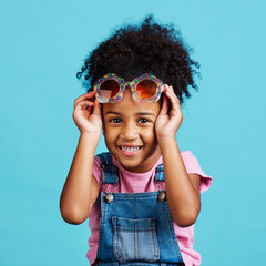 Portrait, funky glasses and girl with smile, excited and cheerful against a blue studio background....
