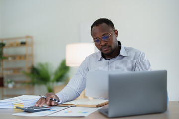 middle age man American African using calculator for calculating and laptop computer with planning...