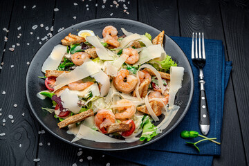 Caesar salad with grilled shrimp on a dark background, top view