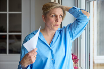 Menopausal Mature Woman Having Hot Flush At Home Cooling Herself With Letters Or Documents