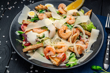 Caesar salad with grilled shrimp on a dark background, top view