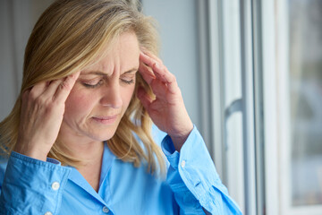 Menopausal Mature Woman At Home Standing By Window Suffering With Headache Or Migraine Pain