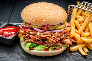Burger with smoked pork and fried french fries on a dark background
