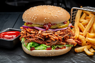 Burger with smoked pork and fried french fries on a dark background