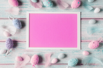 Pink blank card in white frame and decorative eggs over wooden background. Easter holiday greeting