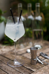 transparent cocktail with two straws in a glass with a stem on a wooden surface