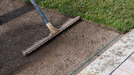 Preparing the soil with a rake for new turf and laying a cable for an automatic  lawn mower robot...