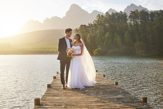 Love, married or romance with a bride and groom on a pier over a forest lake in nature after their ceremony. Wedding, love and water with a young couple in celebration of their marriage outdoor