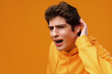 Young man on yellow background hold hand at ear listen to news