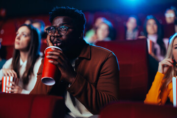 African American man drinking beverage in movie theater.