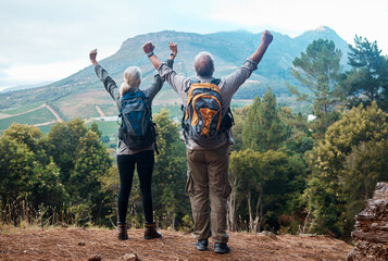 Hiking, mature couple and arms raised on cliff from back on nature walk and mountain in view in...