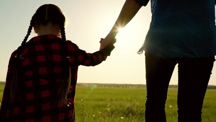 Mother and kid, girl, are walking hand in hand in sun in park together. Happy family, baby daughter, mom hold hands close-up in sun, teamwork. Parent, child, happy childhood. Happy family travel, mama
