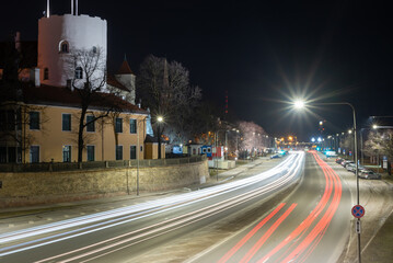 Car light trails at night on a street along the water line in an old city. Riga Old Town. Long...