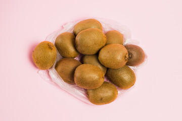 Kiwi in a plastic bag on a pink background. Concept of earth day, zero waste and recycling.