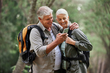 Phone, video call and elderly couple hiking in a forest, happy and smile while bonding on adventure. Active seniors, online and maps for man and woman backpacking in nature while checking location