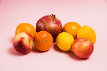 Fruits of pomegranate, lemon, apple, oranges and tangerine on a pink background. Delicious fruits on a bright background.