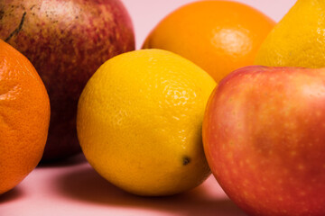 Fruits pomegranate, lemon, apple, oranges and tangerine on a pink background close-up. Delicious fruits on a bright background.