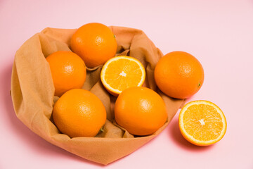 Juicy oranges in a reusable bag for fruits and vegetables on a pink background. Concept of earth day, zero waste and recycling.