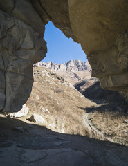An arched opening or tunnel in the rocks through which a mountain landscape opens with peaks with a forest and rocks, in autumn in the mountains