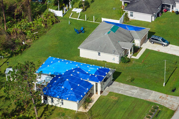 Hurricane Ian damaged house rooftops covered with protective plastic tarp against rain water...