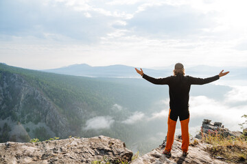 Conquering the mountain alone, a sense of calm, on the top of the mountain stands a guy hands to the sides, the hero of the day on the top of the hill, a traveler on a rock in a hike in nature.