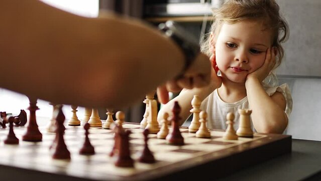 Father teaching his little daughter to play chess at the table in home kitchen. The concept early childhood development and education. Family leisure, communication and recreation.