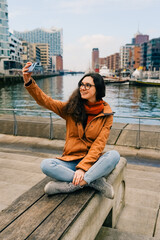 Happy woman taking selfie through smart phone in Hafencity, Hamburg, Germany.