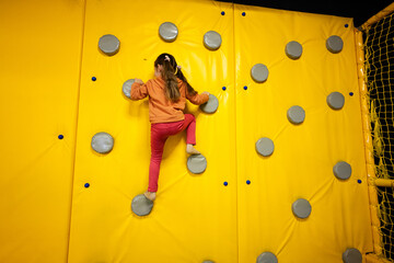 Little girl kid climbing wall at yellow playground park. Child in motion during active entertaiments.