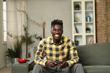 Young happy African guy playing video game at home. Man holding joystick and playing video games.