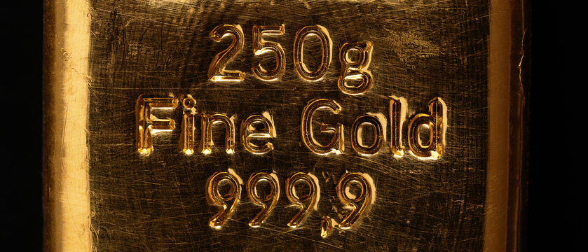 Stamped writing on a cast gold bar, also known as gold bullion. Refined metallic gold, produced by by pouring molten metal into a bar-shaped mold. 250 gram fine gold, equal to 8.04 troy ounces. Photo.