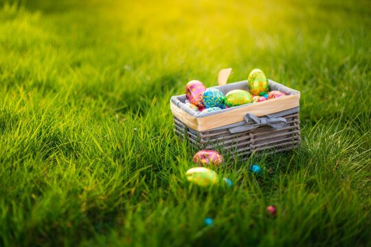 Easter eggs in basket in grass. Colorful decorated easter eggs in wicker basket. Traditional egg hunt for spring holidays. Morning magical light.