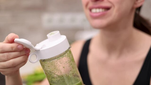 slim woman doing healthy smoothie at kitchen from celery apple kiwi and tangerine fruit.millennial female pressing blender button, drinking or sitting with cup in front of belly.postpartum recovery