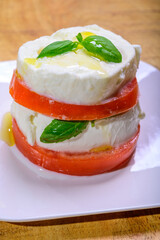Sliced white ball of Italian soft cheese Mozzarella di Bufala Campana served with fresh green basil and red tomato